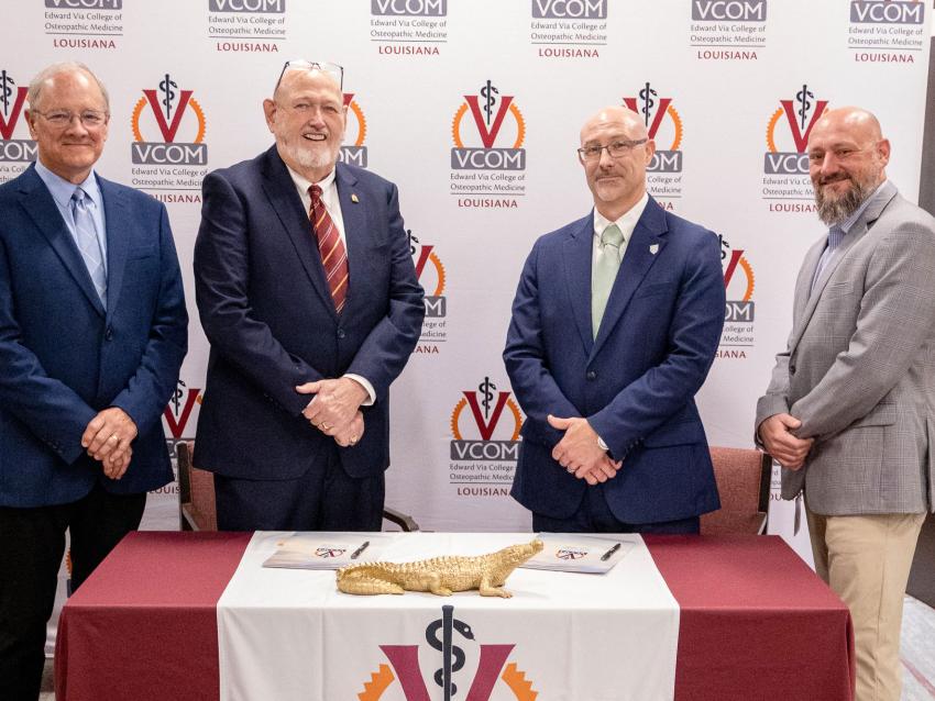 Representatives from VCOM and FranU standing in front of a signing table smiling