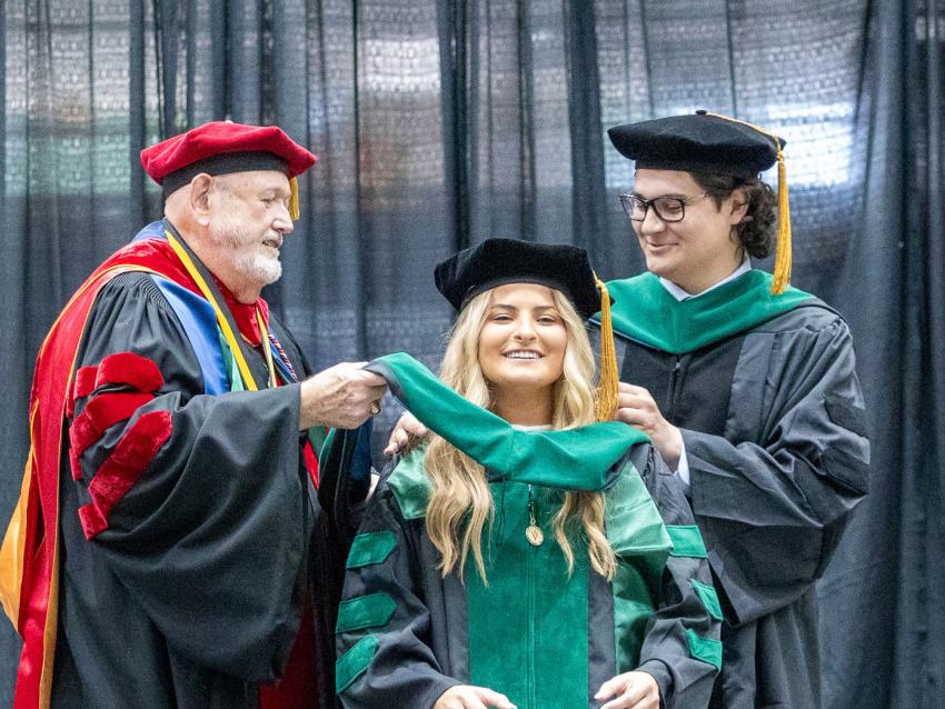 VCOM Louisiana class of 2026 graduate being hooded on stage by two other doctors