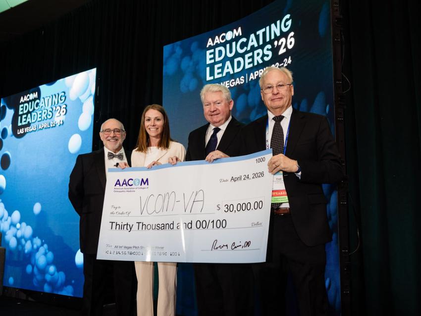 Representatives from VCOM standing on a stage holding a large check