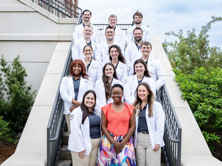 Jasmine Belton and VCOM-Louisiana students in white coats standing outside on a staircase smiling.
