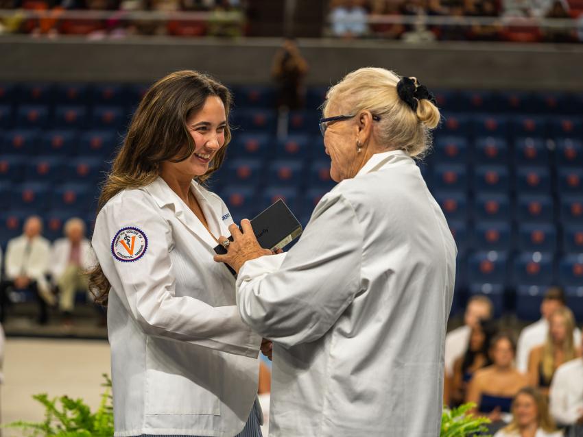 Dr Tooke-Rawlins handing a Butterfly Network portable ultrasound device to a medical student in a white coat on a stage