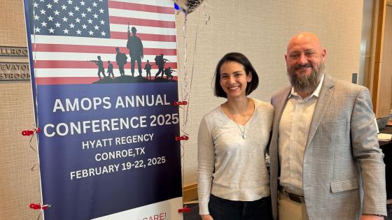 Sydney Gould standing in front of AMOPS Conference poster