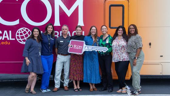 VCOM-Carolinas faculty standing in front of a mobile medical unit holding an oversized key