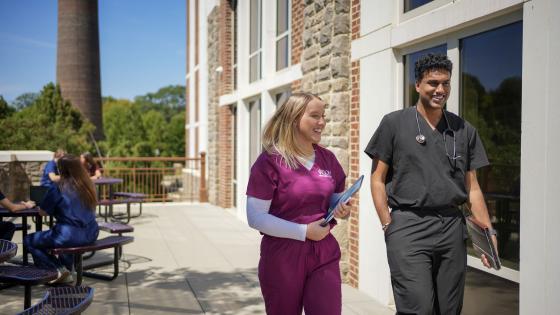 Two VCOM-Carolinas students in scrubs walking and smiling.