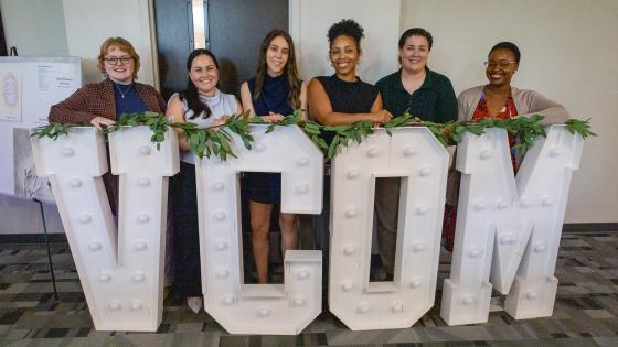 VCOM-Louisiana students gathered around a giant VCOM light up sign