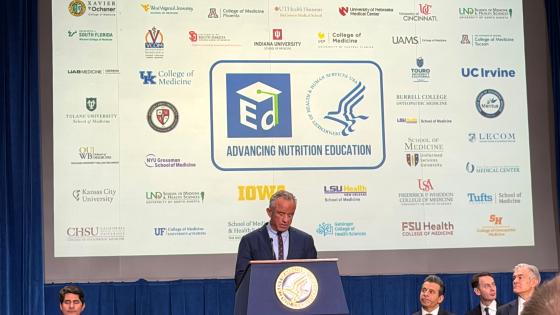 RFK Jr speaking in front of a screen of medical school logos