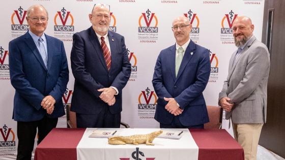 Representatives from VCOM and FranU standing in front of a signing table smiling