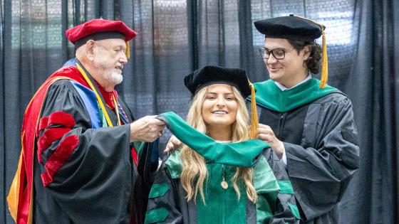 VCOM Louisiana class of 2026 graduate being hooded on stage by two other doctors