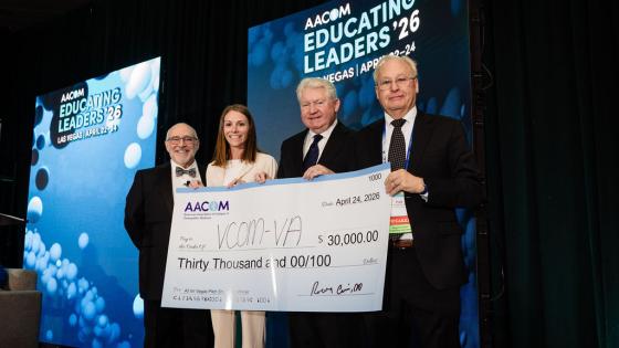 Representatives from VCOM standing on a stage holding a large check