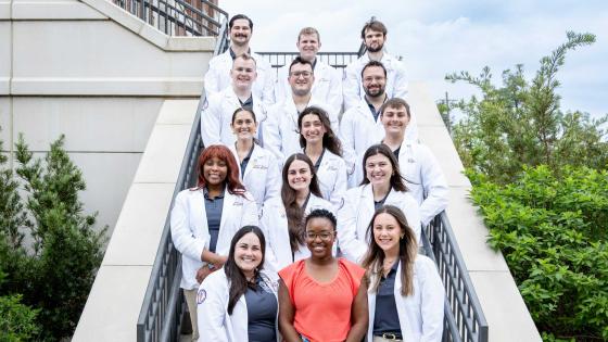 Jasmine Belton and VCOM-Louisiana students in white coats standing outside on a staircase smiling.