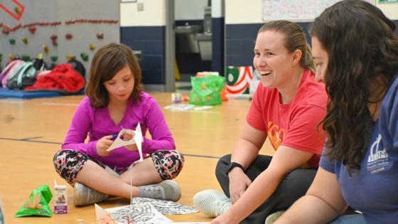 Medical student sitting on the floor with child working on a paper brain project