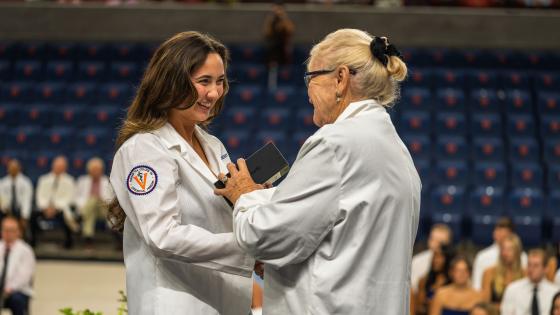 Dr Tooke-Rawlins handing a Butterfly Network portable ultrasound device to a medical student in a white coat on a stage